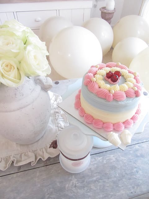 A pastel layer cake with piped pink frosting beside a Sugared Sweet Scents candle and white roses
